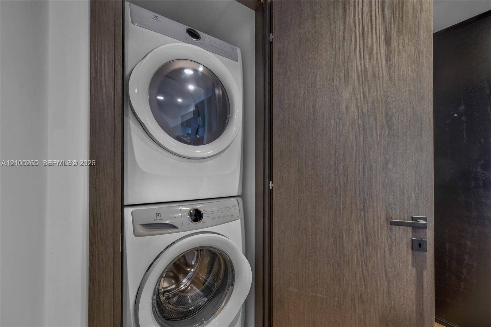 398 NE 5th Street, #2219, Miami, FL 33132 Stacked white front-load washer and dryer unit enclosed in a closet with a full-height, dark wood-finish door and integrated metal lever handle