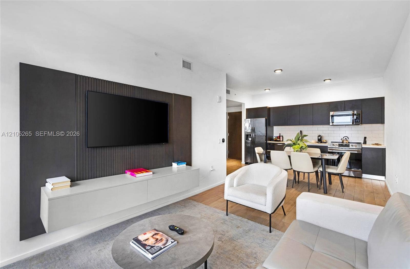 398 NE 5th Street, #2219, Miami, FL 33132 Living area featuring a custom dark-toned ribbed media wall with a built-in light gray floating console, complemented by wood-finish flooring and kitchen cabinetry finished in a dark stain with a subway tile backsplash