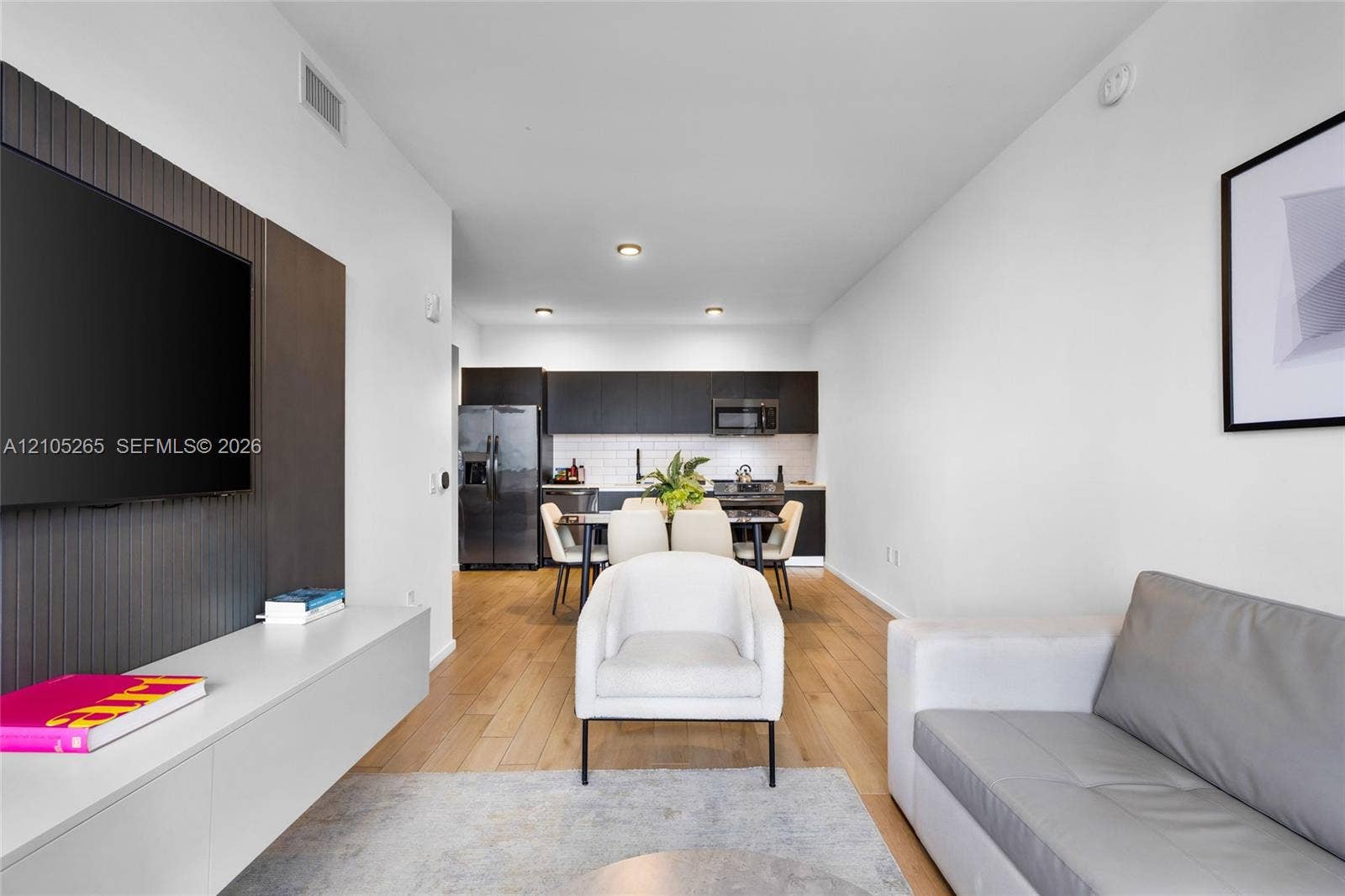 398 NE 5th Street, #2219, Miami, FL 33132 Modern interior featuring wood-finish flooring, a matte-finish accent wall with a wall-mounted media console, dark cabinetry, and white tile backsplash