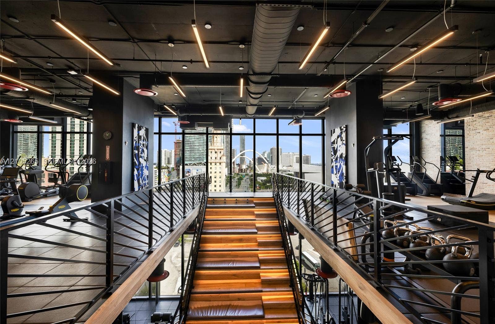 398 NE 5th Street, #2219, Miami, FL 33132 Industrial-style fitness center featuring an open-concept layout, floor-to-ceiling glass windows, exposed ductwork, wood-tread staircase with integrated lighting, and matte black metal railings