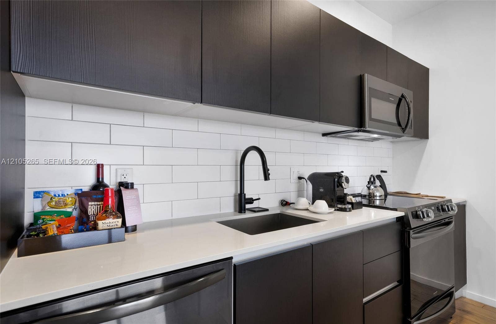 398 NE 5th Street, #2219, Miami, FL 33132 Modern kitchen featuring dark slab-style cabinetry, light-toned countertops, white subway tile backsplash, matte black hardware, and stainless steel appliances