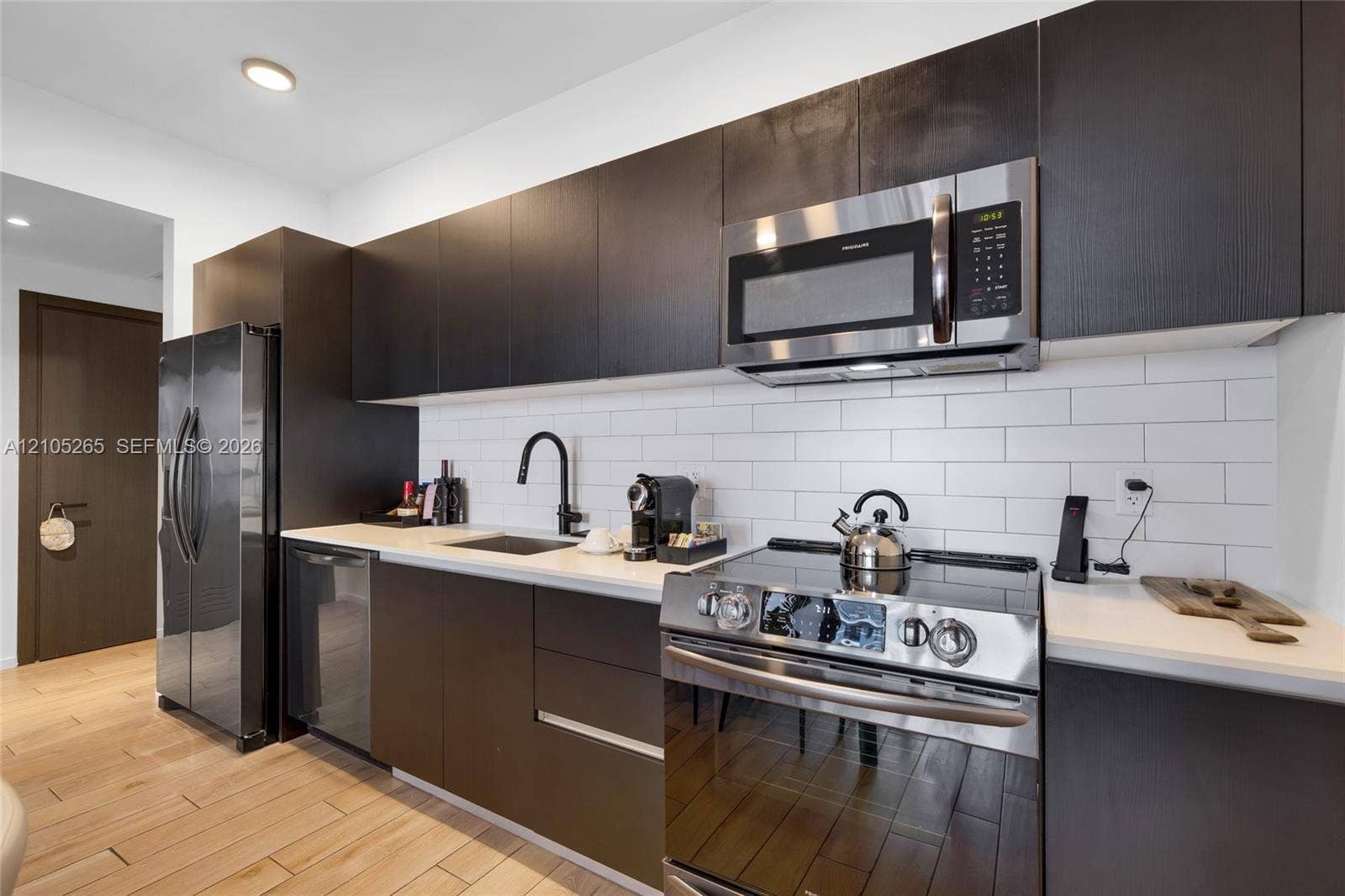 398 NE 5th Street, #2219, Miami, FL 33132 Modern kitchen featuring dark cabinetry, white subway tile backsplash, solid-surface countertops, stainless steel appliances, and wood-finish flooring