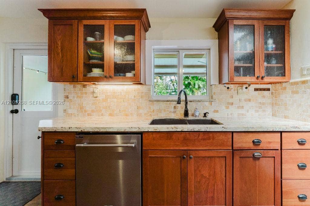 230 Miami Springs Avenue, Miami Springs, FL 33166 Wood cabinetry with glass-front upper cabinets, stainless steel dishwasher, speckled countertops, and a mosaic tile backsplash