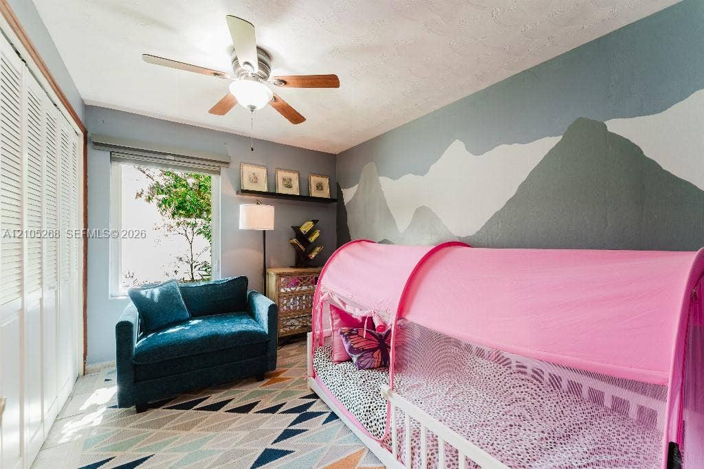 230 Miami Springs Avenue, Miami Springs, FL 33166 Louvered bifold closet doors, window with roller shade, ceiling fan with light fixture, and a wall-mounted shelf