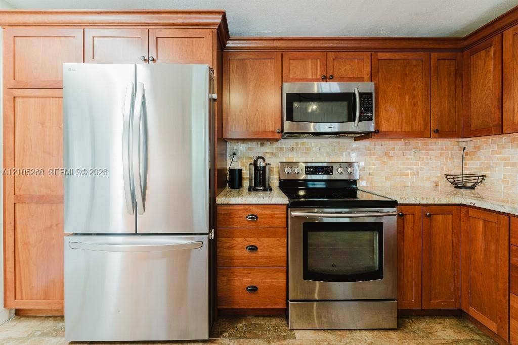 230 Miami Springs Avenue, Miami Springs, FL 33166 Stainless steel French door refrigerator, wood cabinetry, stainless steel microwave, stainless steel electric range, and light-toned mosaic tile backsplash