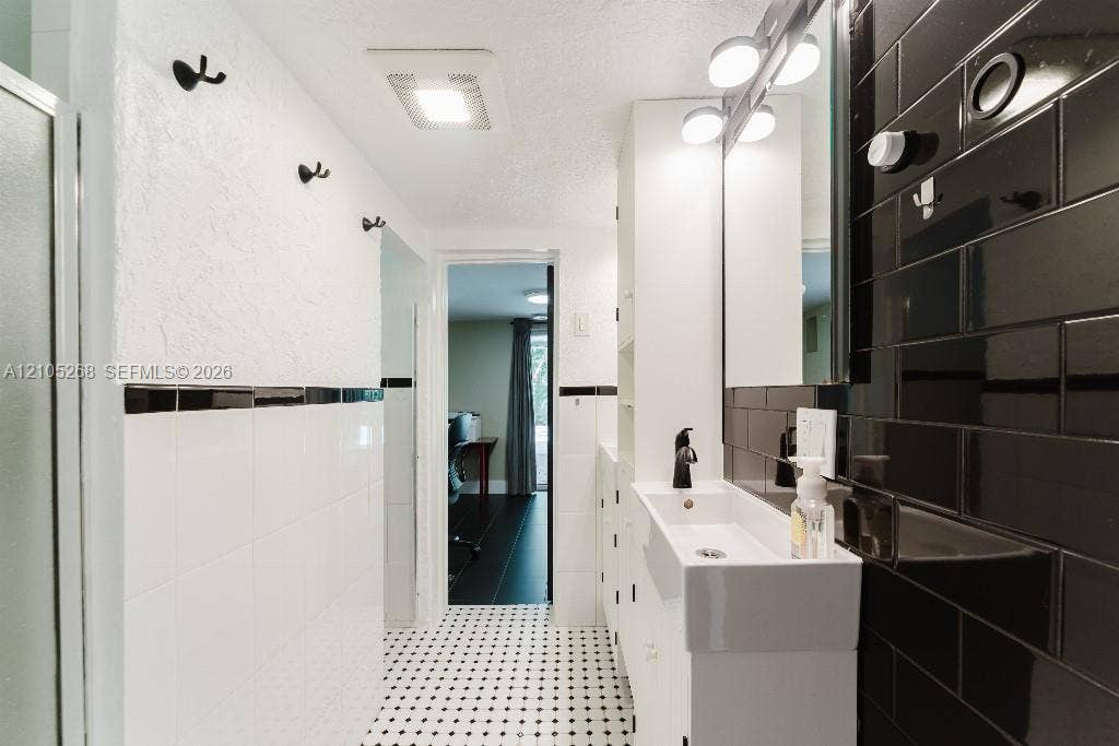 230 Miami Springs Avenue, Miami Springs, FL 33166 Black and white tile flooring, white subway tile wainscoting, black subway tile accent wall, contemporary vanity with integrated sink, and matte black faucet