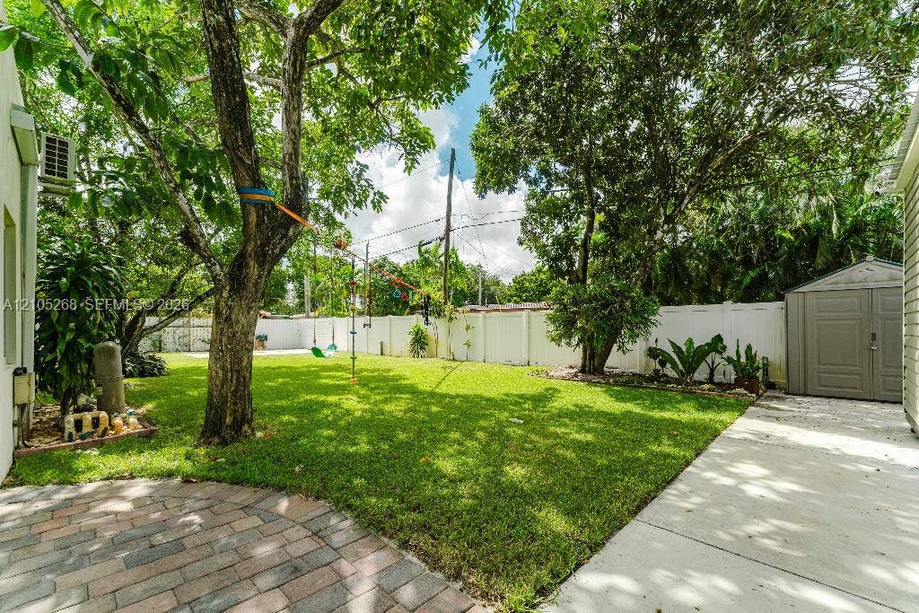 230 Miami Springs Avenue, Miami Springs, FL 33166 Manicured lawn, mature trees, white privacy fencing, paved patio area, and a storage shed