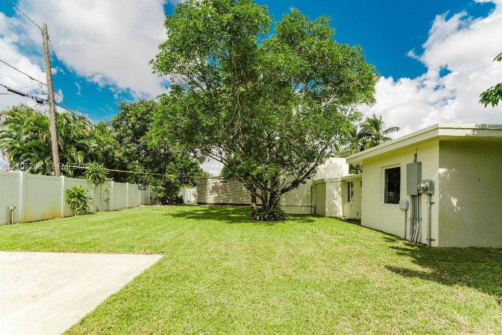 230 Miami Springs Avenue, Miami Springs, FL 33166 Expansive grass lawn with a mature central tree, concrete patio, and perimeter fencing