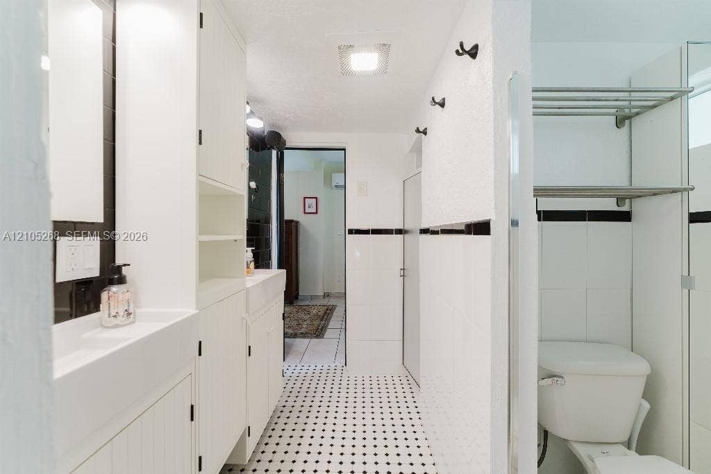 230 Miami Springs Avenue, Miami Springs, FL 33166 Black and white mosaic tile flooring, built-in white cabinetry, integrated sink, white tiled walls with black accent banding, and a white toilet
