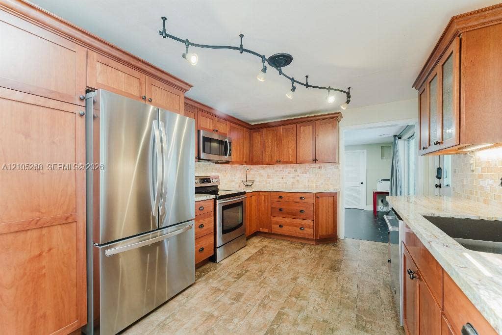 230 Miami Springs Avenue, Miami Springs, FL 33166 Kitchen featuring warm wood cabinetry, stainless steel appliances, light-toned backsplash, granite countertops, and track lighting