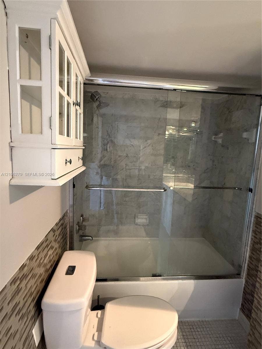 Tub and shower combination with glass enclosure, subway tile surround, mosaic tiled wall, and built-in white cabinetry