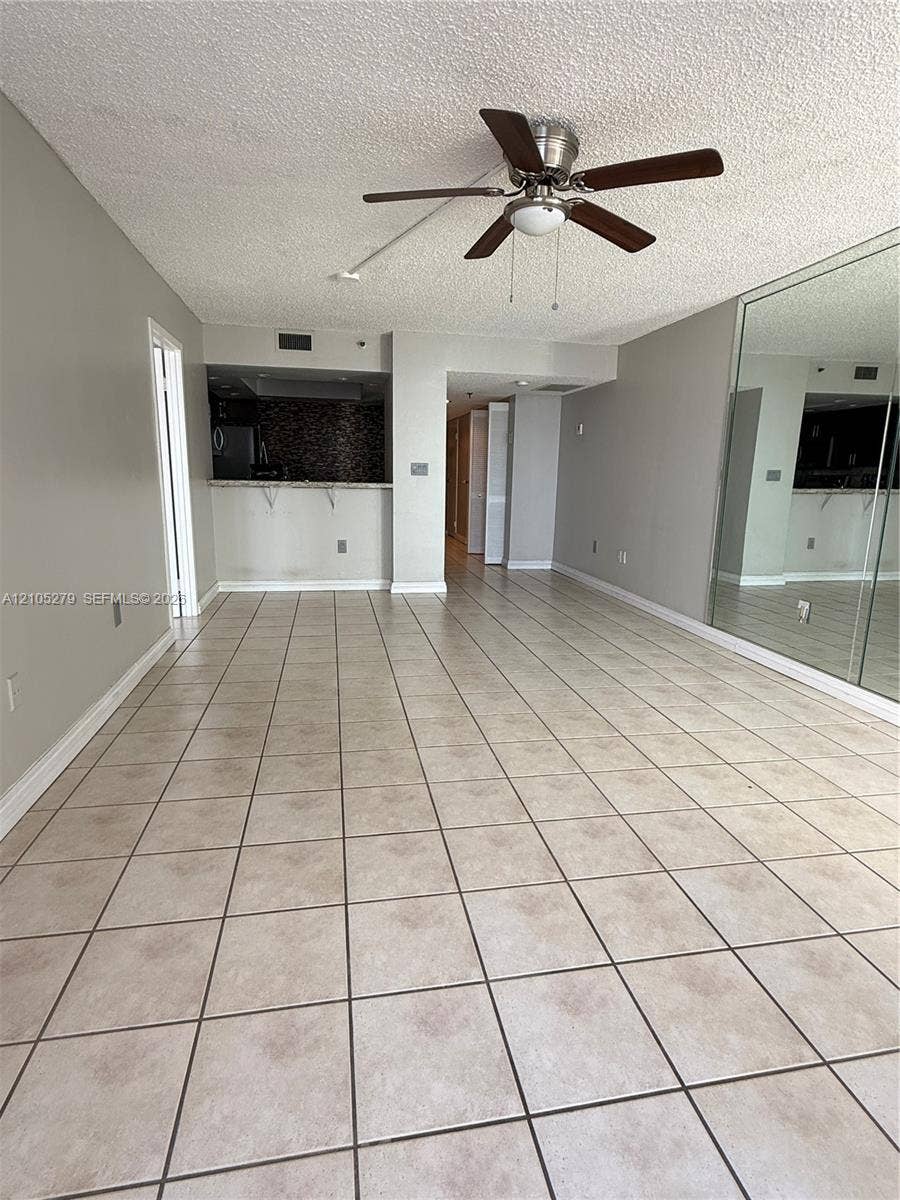 Tiled flooring throughout, featuring a ceiling fan with integrated lighting, mirrored wall panels, and a kitchen pass-through with a tiled backsplash