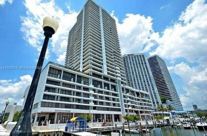 Waterfront high-rise building featuring multiple balconies, a lower-level commercial space, and a marina with boat slips