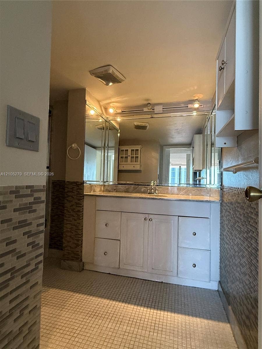 White vanity with dual cabinets and four drawers, mosaic tile flooring, and track lighting