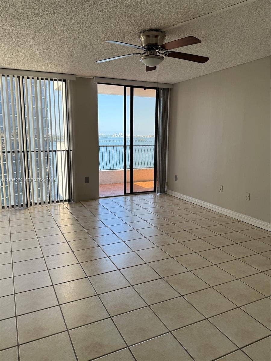 Expansive tiled flooring, direct balcony access, ceiling fan with light fixture, and vertical blinds