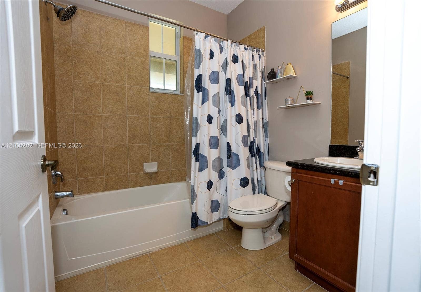 1104 SW 146th Terrace, Pembroke Pines, FL 33027 Bathroom featuring a tub-shower combination with floor-to-ceiling tile surround, dark-toned vanity with a contrasting solid surface countertop, inset sink, and built-in wall shelving