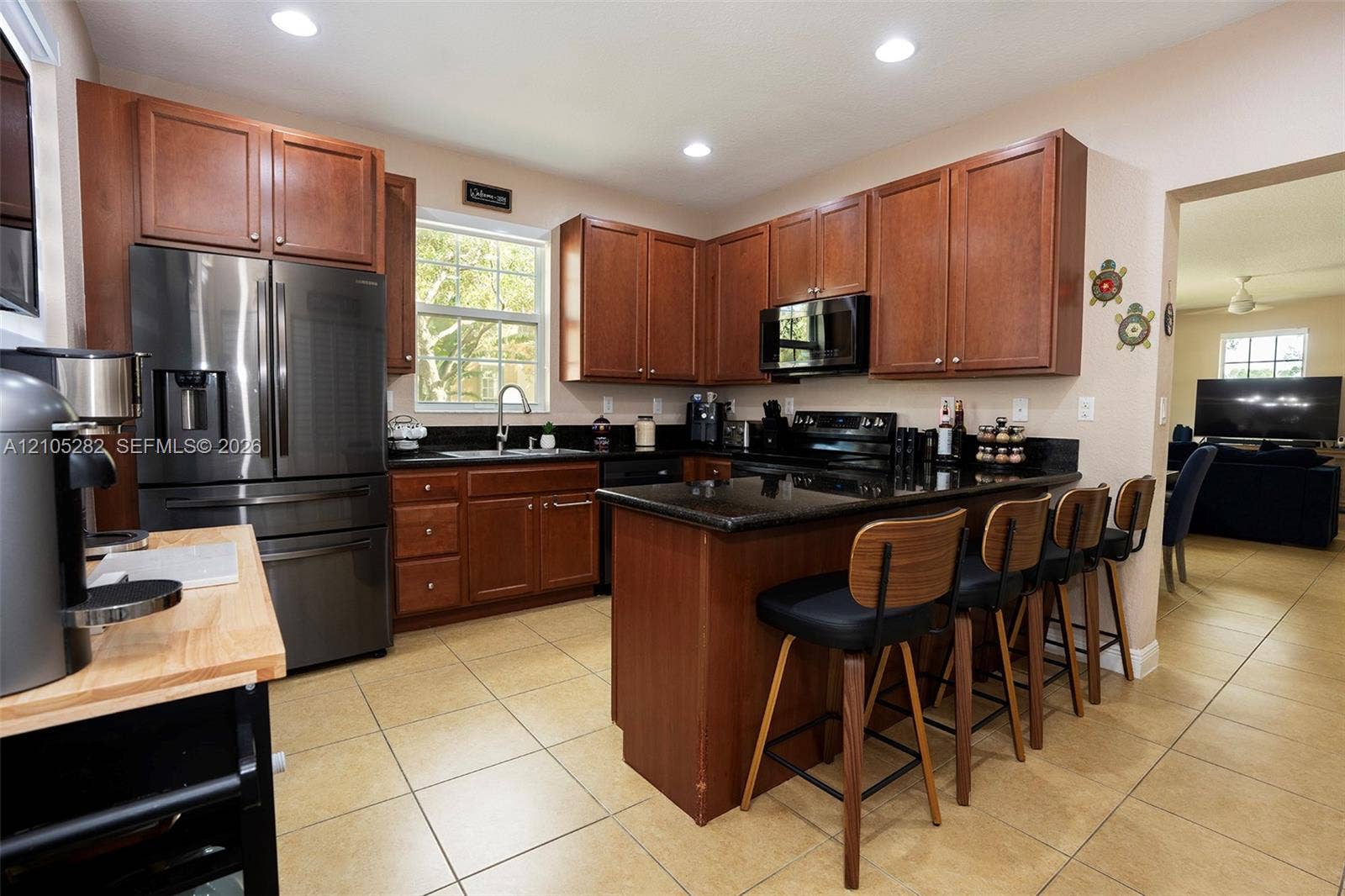 1104 SW 146th Terrace, Pembroke Pines, FL 33027 Kitchen featuring rich-tone wooden cabinetry, dark stone countertops, stainless steel appliances, a breakfast bar, and tile flooring