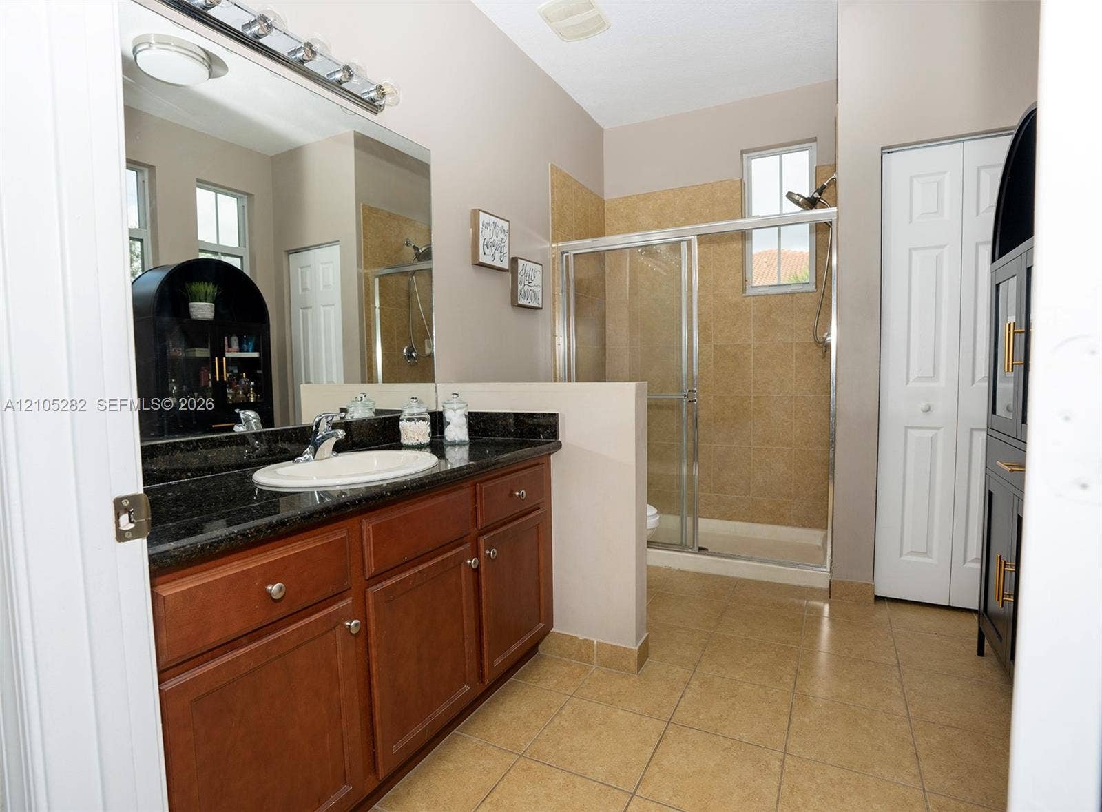 1104 SW 146th Terrace, Pembroke Pines, FL 33027 Bathroom featuring dark stone-surface vanity with an integrated oval sink, wood-finish cabinetry, tile flooring, and a walk-in shower with tiled surround and glass enclosure