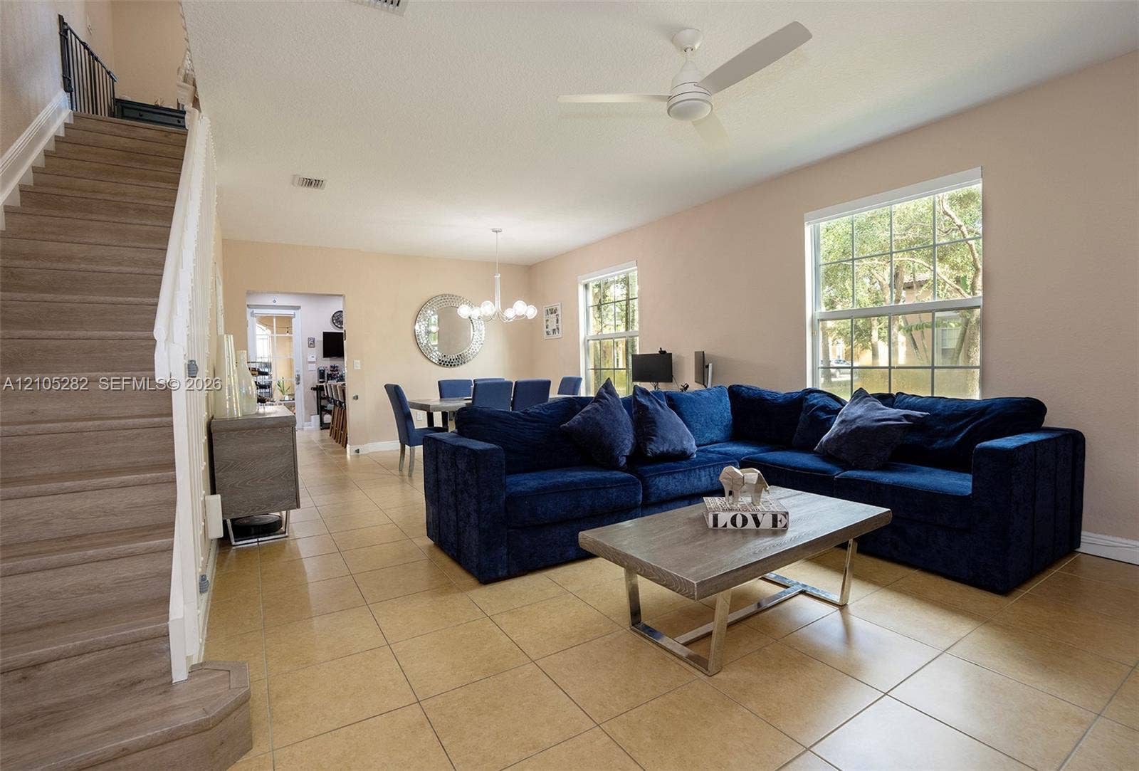 1104 SW 146th Terrace, Pembroke Pines, FL 33027 Open-concept interior featuring large-format tile flooring, wood-finish staircase, multi-arm chandelier, and white ceiling-mounted fan