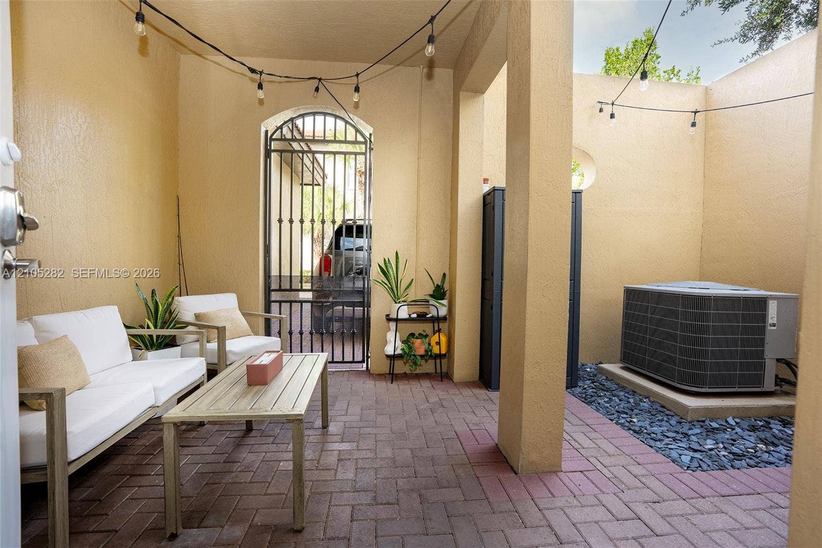 1104 SW 146th Terrace, Pembroke Pines, FL 33027 Covered patio featuring red brick paver flooring, a decorative arched wrought-iron gate, and built-in string lighting