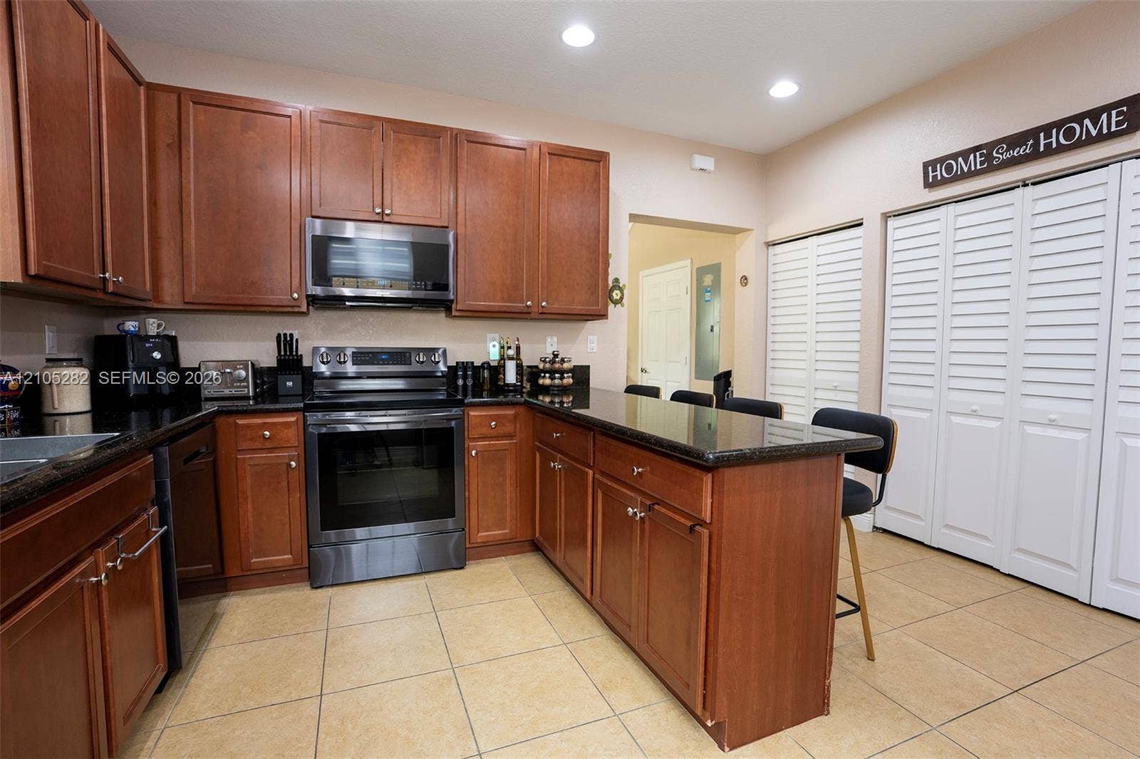 1104 SW 146th Terrace, Pembroke Pines, FL 33027 Kitchen featuring wood cabinetry, dark stone countertops, integrated stainless steel appliances, ceramic tile flooring, and white louvered closet doors