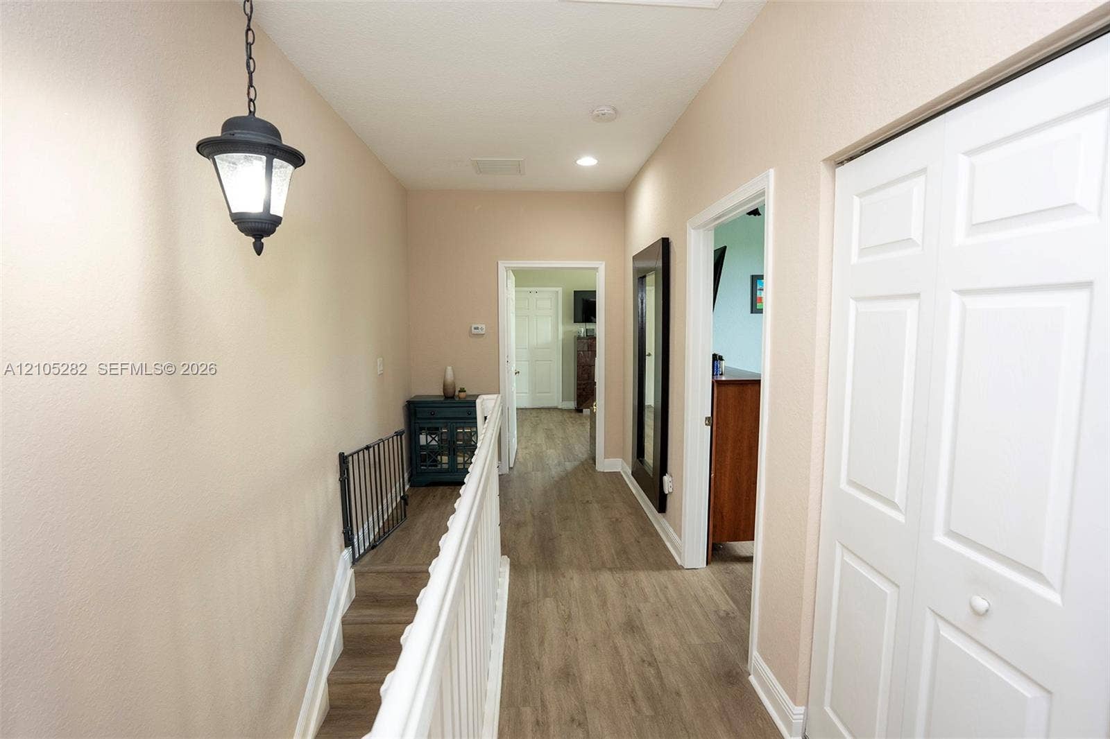 1104 SW 146th Terrace, Pembroke Pines, FL 33027 Hallway featuring wood-finish flooring, a hanging lantern-style light fixture, white wood-slat railing, and bifold closet doors