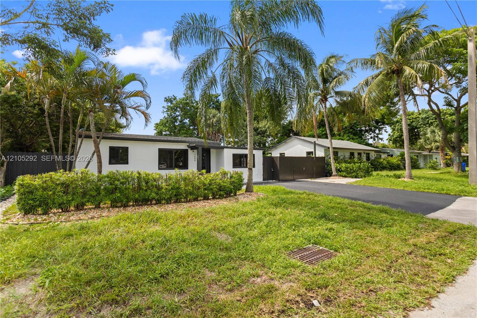White exterior with dark-framed windows, surrounded by mature palm trees and lush landscaping