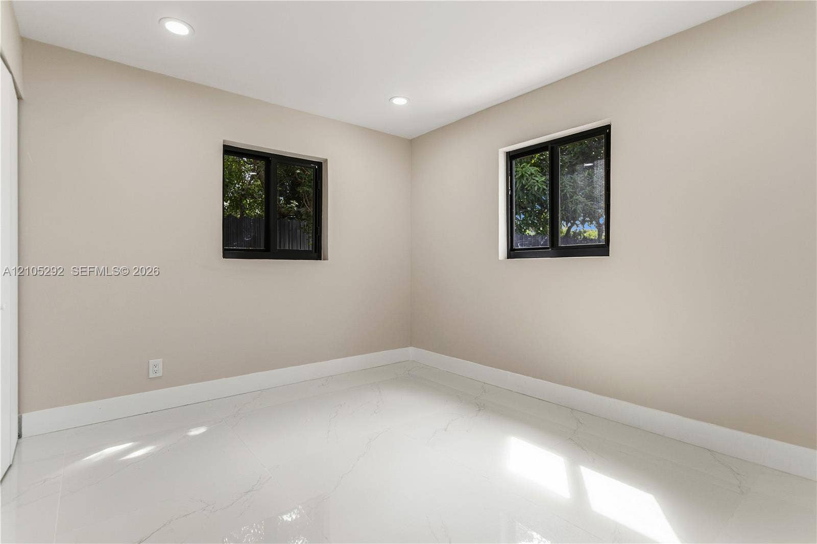 Recessed ceiling lighting, two windows with dark frames, light-toned walls, and white tile flooring