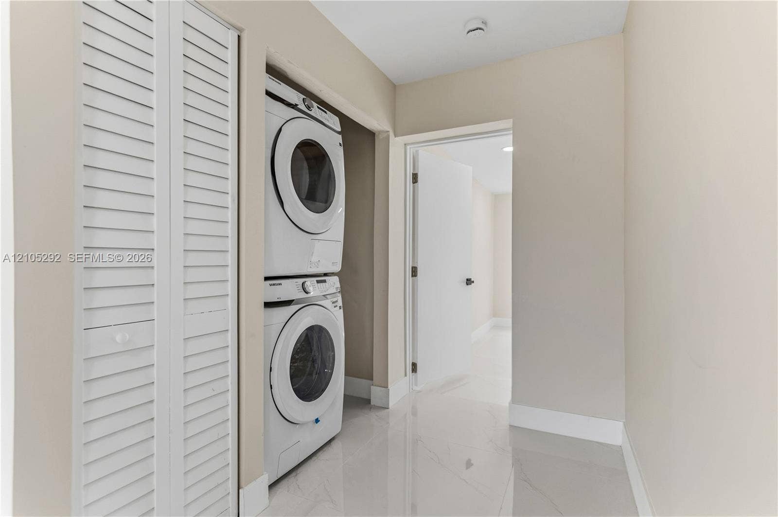 Laundry closet featuring a stacked washer and dryer, white louvered bifold doors, and a tiled floor