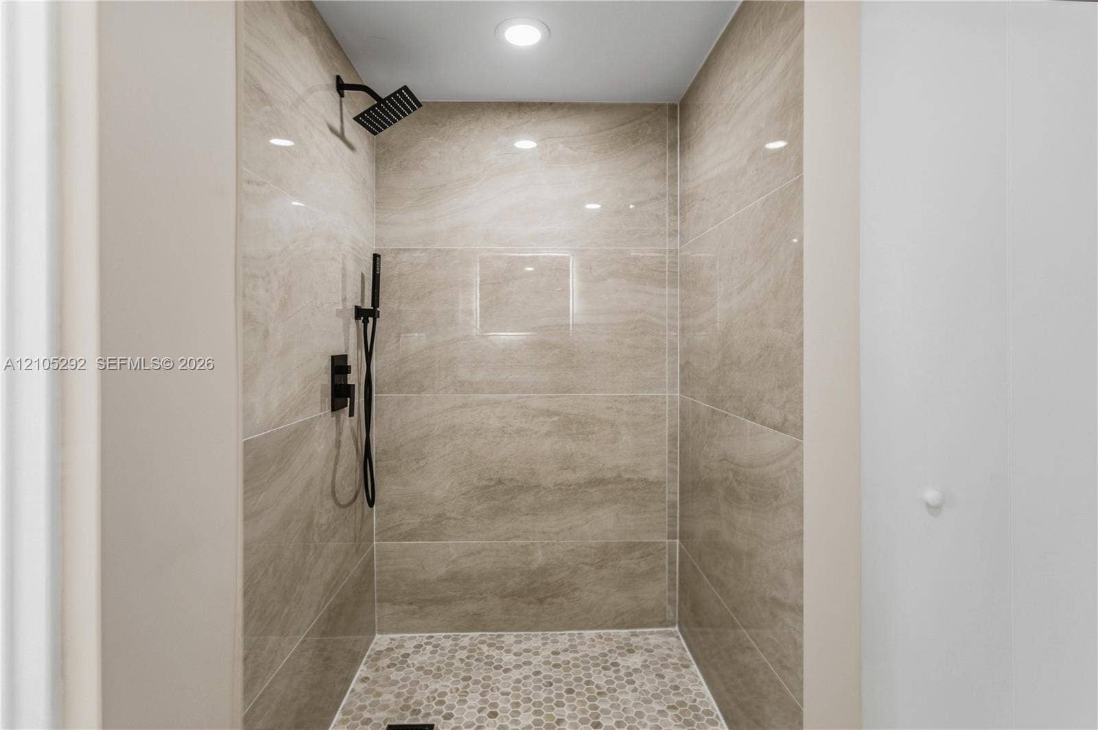 Walk-in shower with large-format wall tiles, hexagonal floor tiles, and matte black shower fixtures