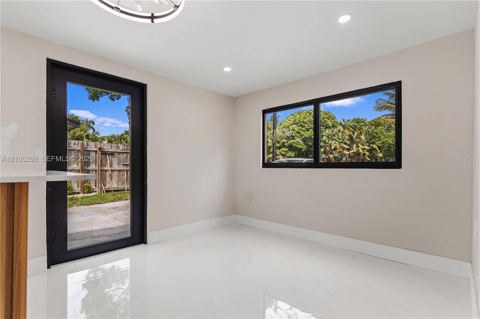 Recessed lighting, wood-finish cabinetry, bright white flooring, black-framed glass door, and black-framed window