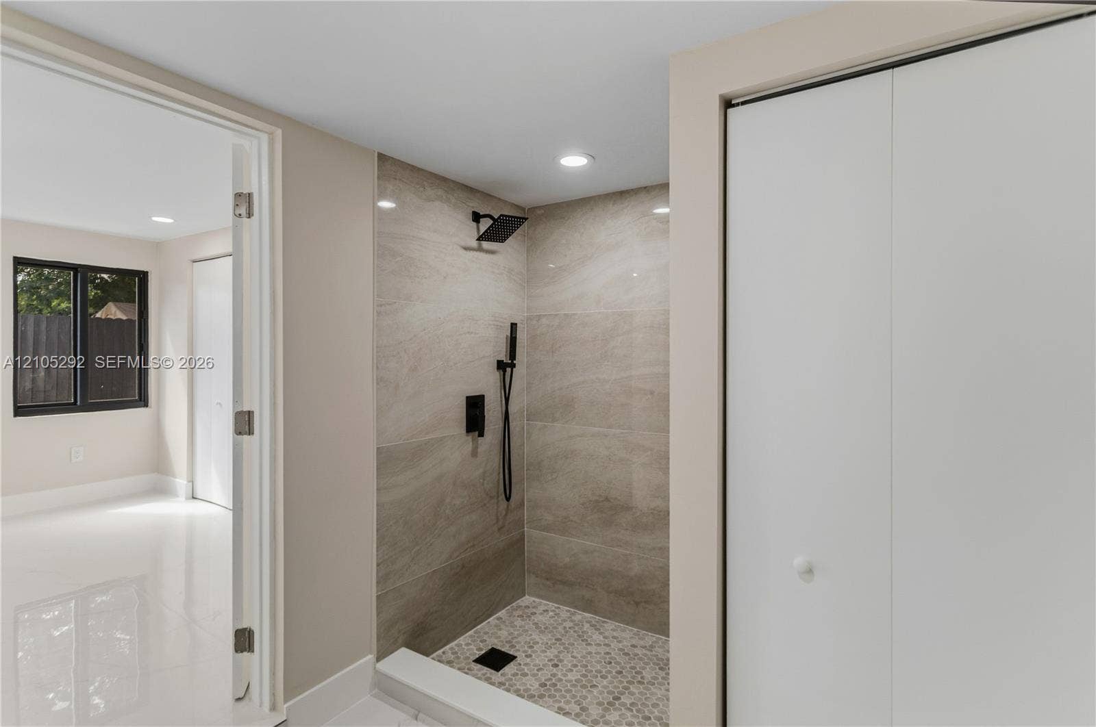 Walk-in shower with tiled walls and floor, featuring matte black fixtures and recessed lighting
