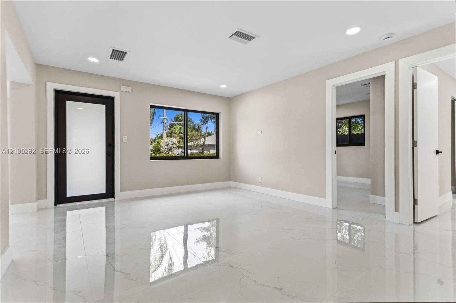 Spacious room featuring polished tile flooring, recessed lighting, a modern entry door with a frosted glass panel, and large windows