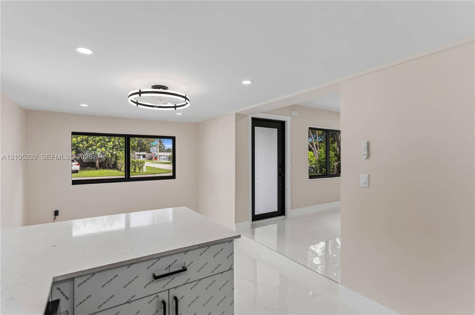 Sleek kitchen island with a light-colored countertop and dark hardware, complemented by recessed lighting and a modern circular light fixture