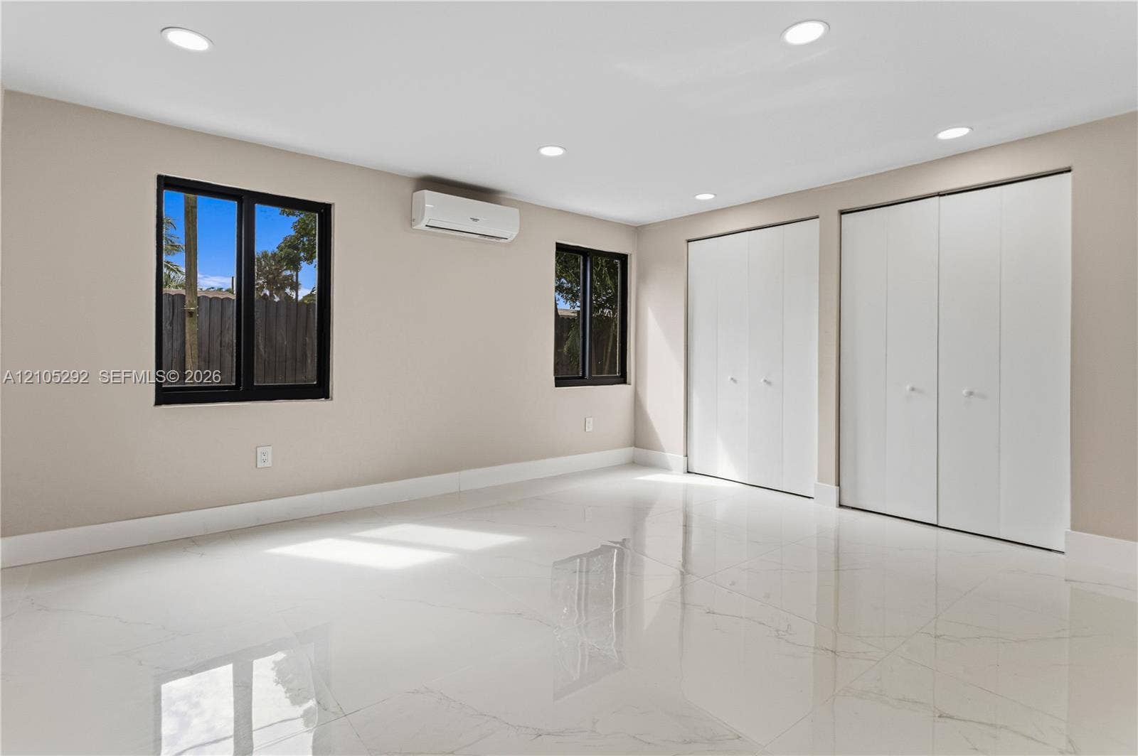 Recessed lighting, light-toned walls, white tile flooring, two windows with black frames, and two sets of bi-fold closet doors