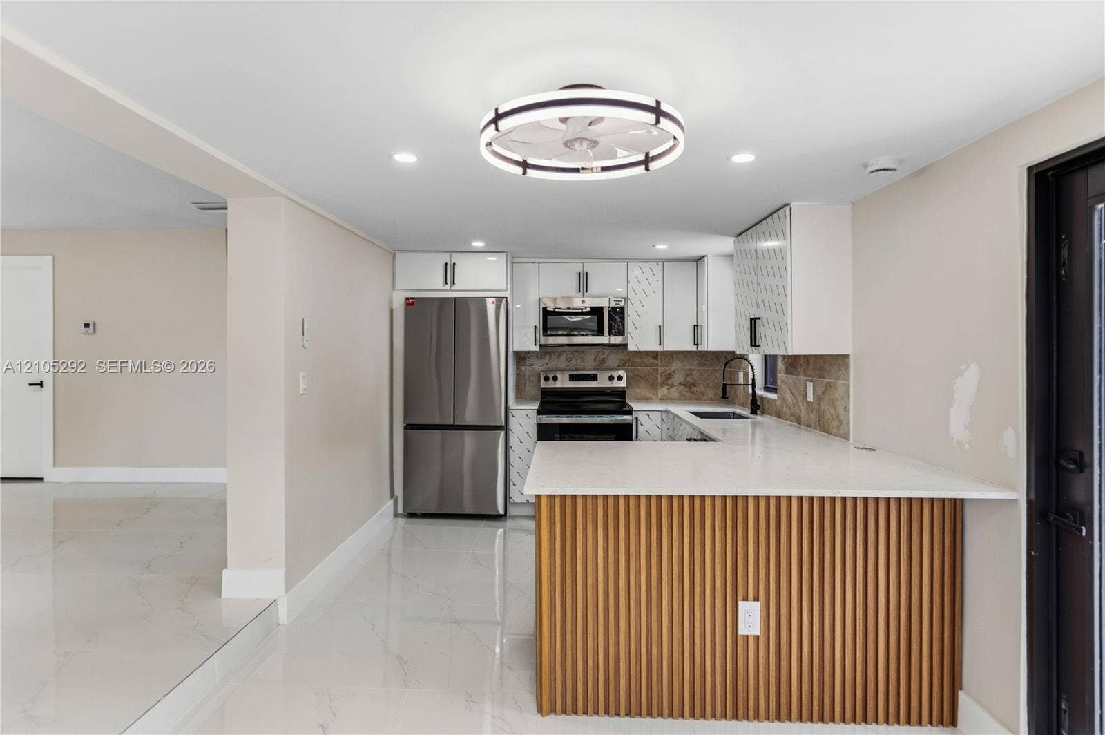 Kitchen with white cabinetry, stainless steel appliances, a tile backsplash, and a breakfast bar with a wood-slat base