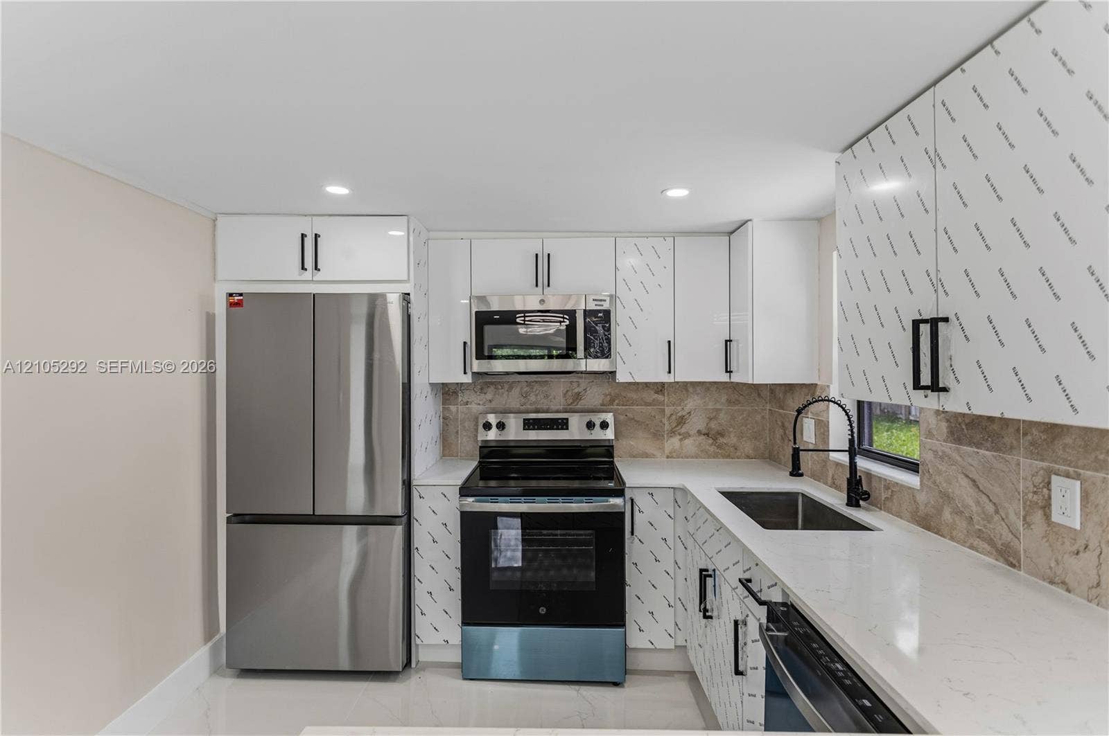 Stainless steel refrigerator, integrated microwave, built-in range, single basin sink with a matte black faucet, and white countertops
