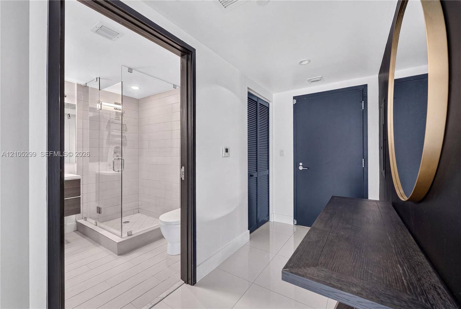 Contemporary bathroom featuring a glass-enclosed shower, wood-finish vanity, and white tile flooring