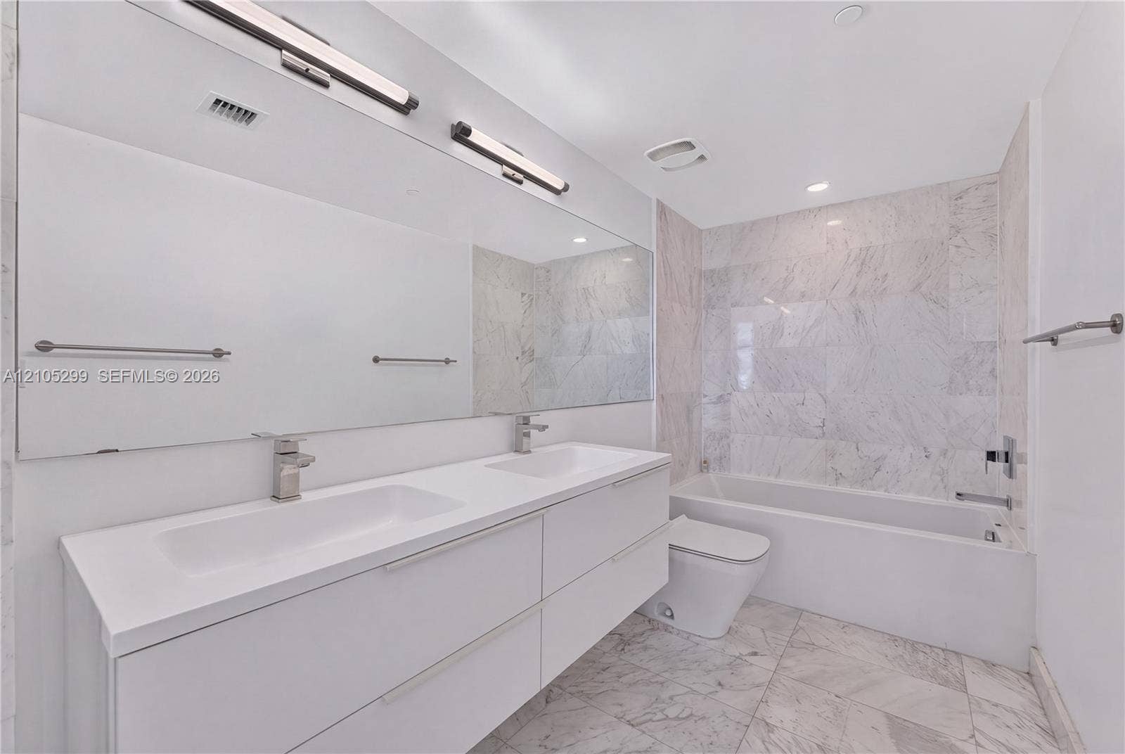 Dual-sink vanity with under-mount sinks, a wide mirror, a tub with a tiled surround, and tiled flooring