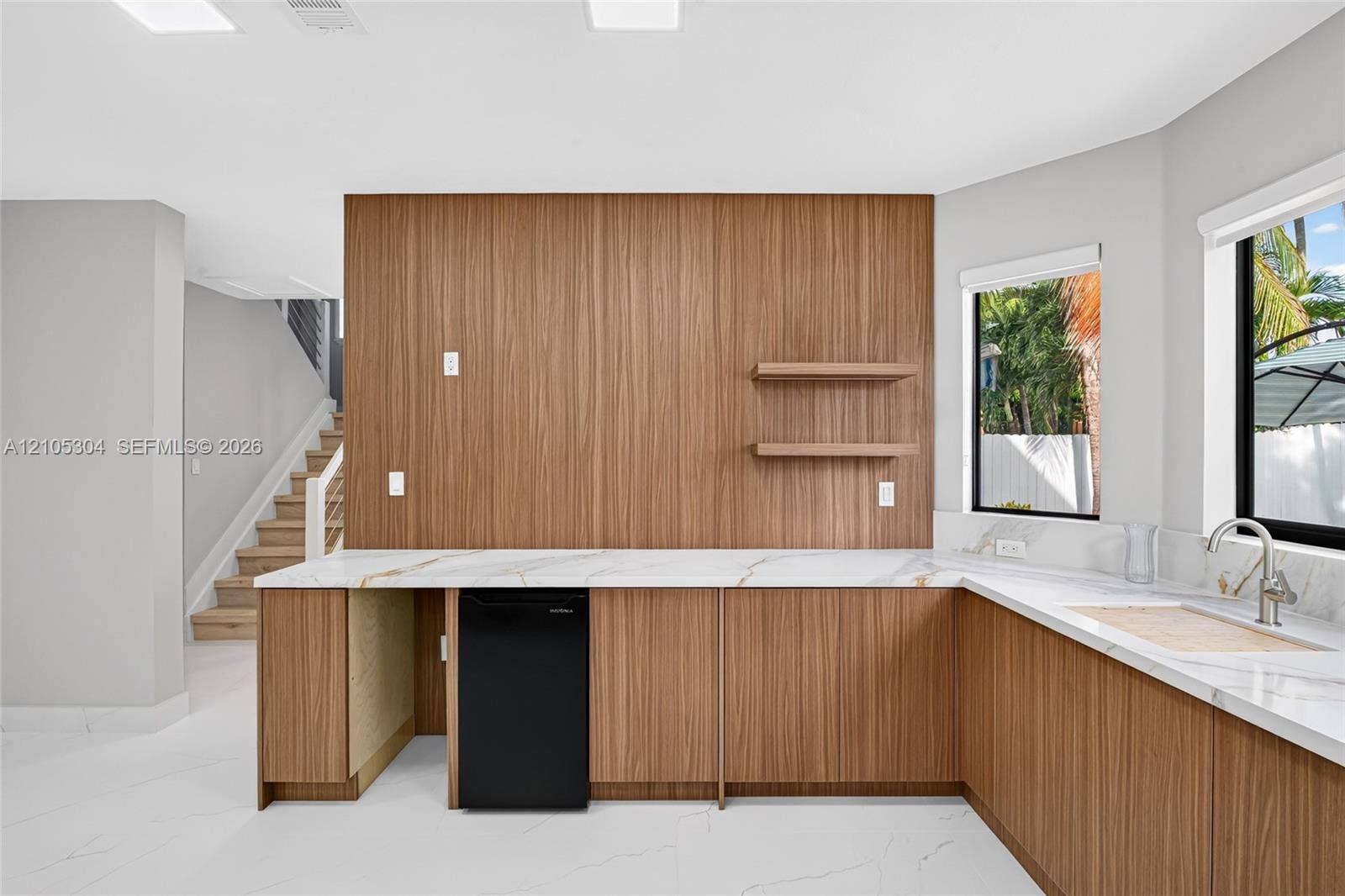 15217 SW 36th Terrace, Miami, FL 33185 Custom wet bar featuring wood-veneer cabinetry, stone-finish countertops, floating shelving, an undermount sink with a gooseneck faucet, and integrated beverage refrigeration