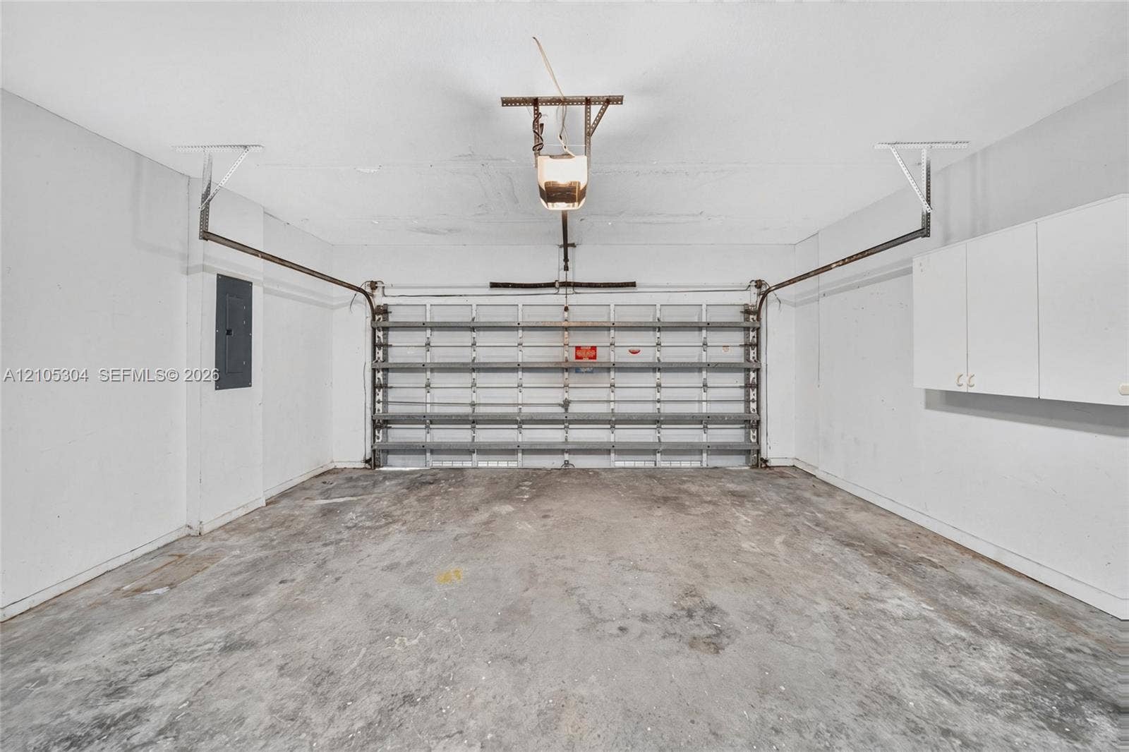 15217 SW 36th Terrace, Miami, FL 33185 Two-car garage featuring a concrete floor, motorized sectional garage door, white wall-mounted storage cabinetry, and an electrical service panel