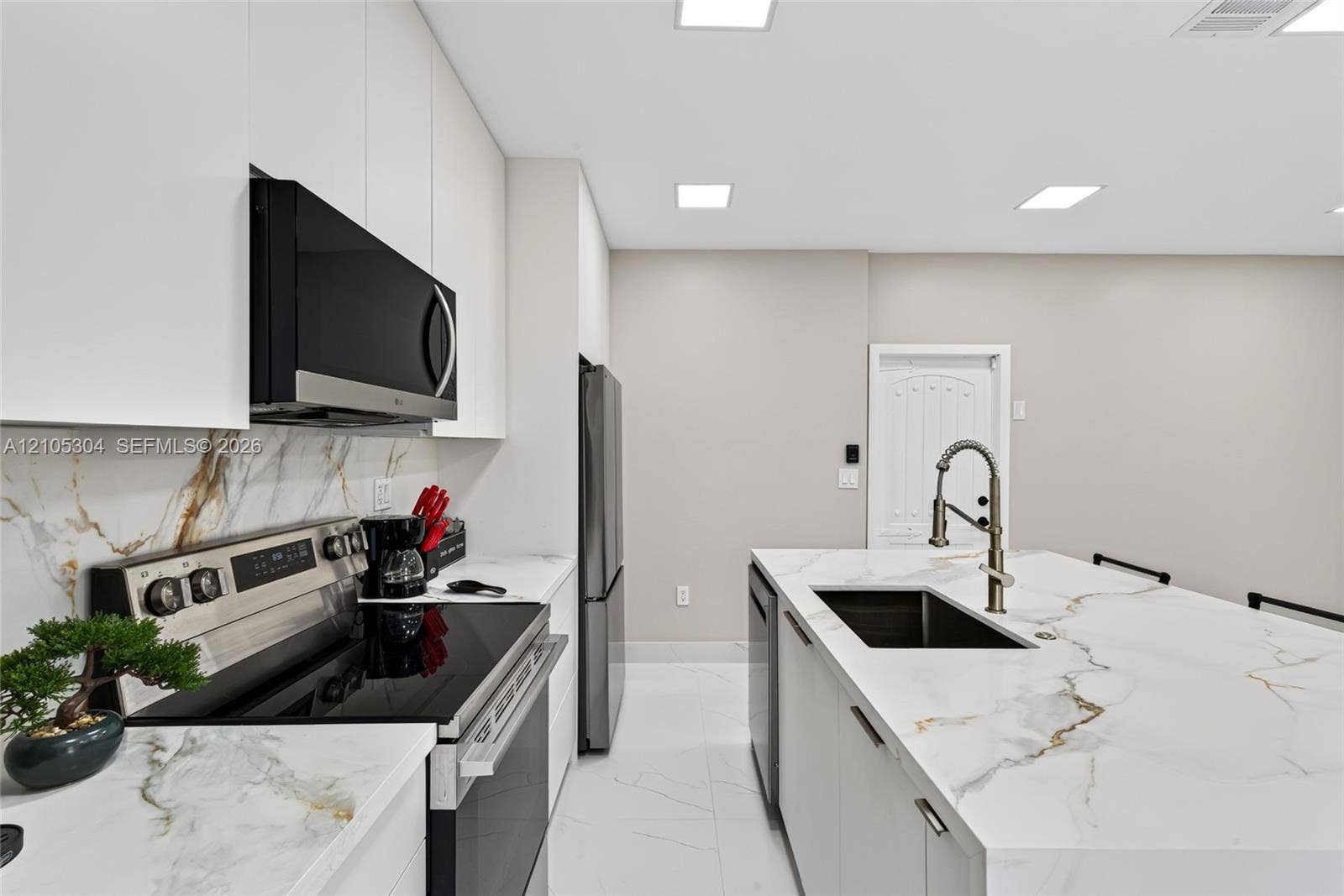 15217 SW 36th Terrace, Miami, FL 33185 Kitchen featuring white slab cabinetry, large-format tiled flooring, stone-finish countertops with matching full-height backsplash, stainless steel appliances, and a central island with a high-arc faucet
