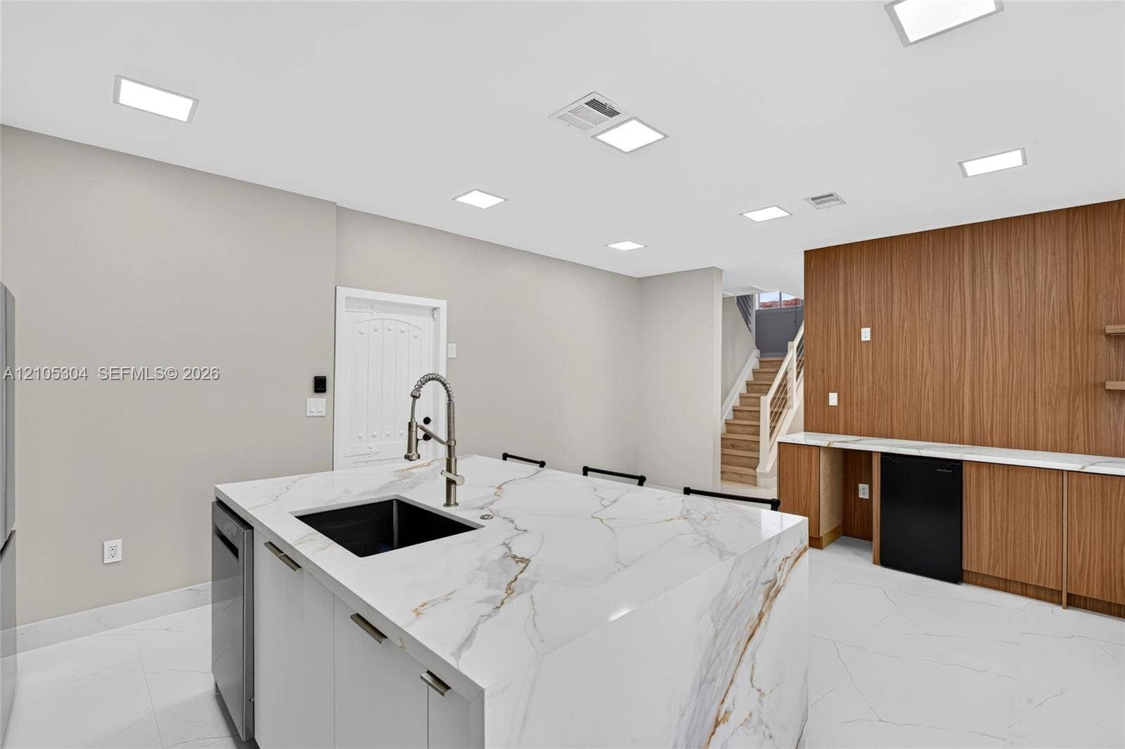 15217 SW 36th Terrace, Miami, FL 33185 Kitchen island with stone-finish waterfall countertop and undermount sink, recessed lighting, wood-finish wall paneling, built-in cabinetry, and tile flooring