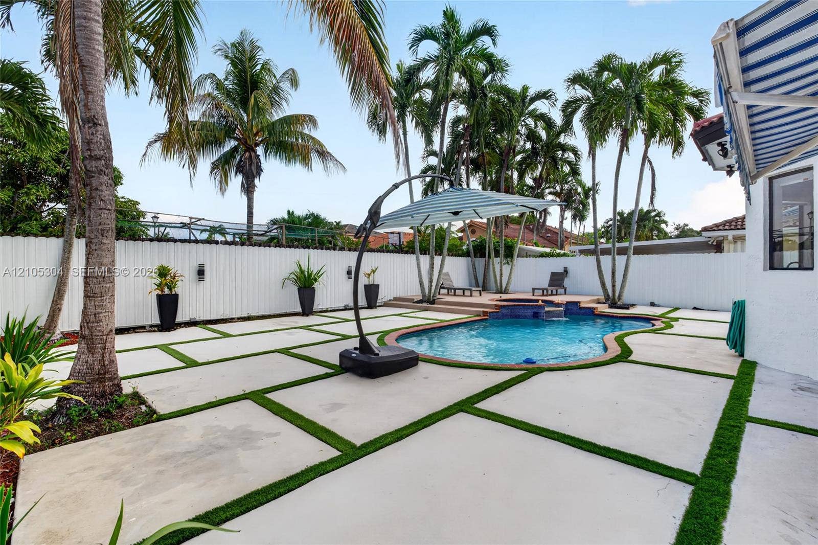 15217 SW 36th Terrace, Miami, FL 33185 Outdoor living area featuring a swimming pool with a raised spa, concrete paver patio with turf inlays, privacy fencing, and mature palm trees