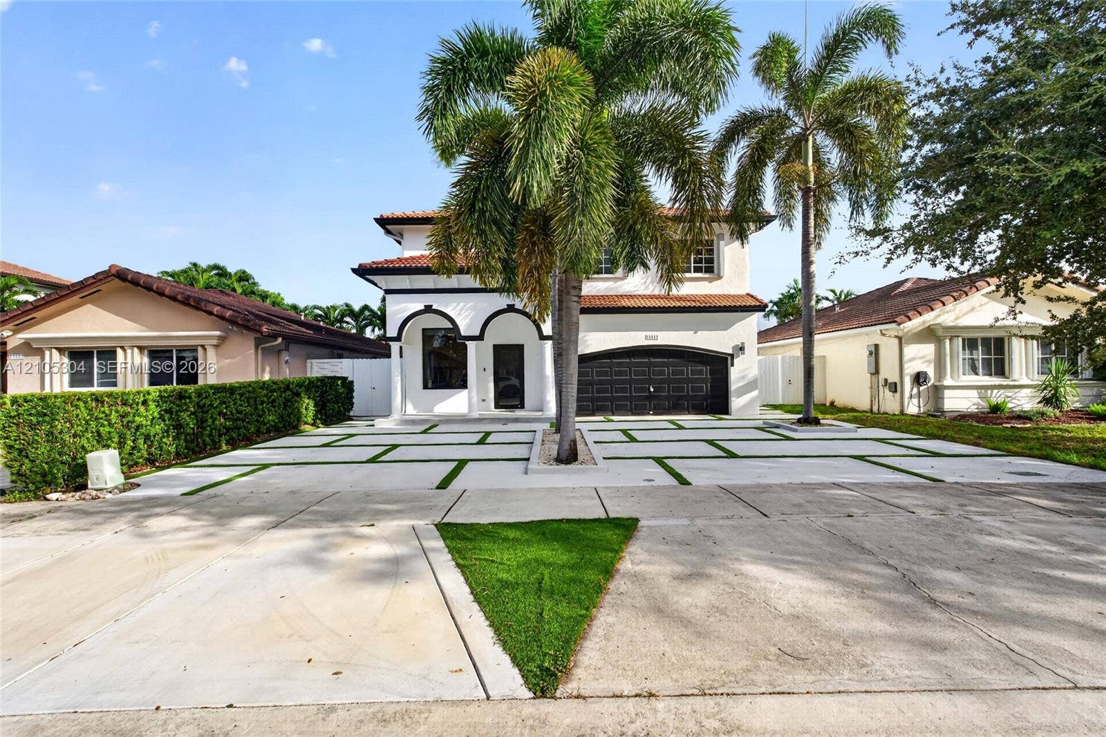 15217 SW 36th Terrace, Miami, FL 33185 Two-story exterior featuring a clay tile roof, arched entryway, multi-panel garage door, and a geometric concrete paver driveway with turf accents