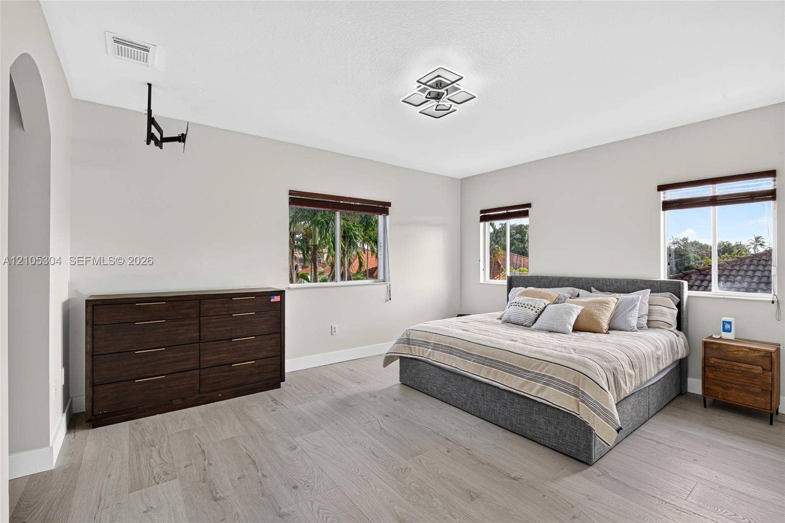 15217 SW 36th Terrace, Miami, FL 33185 Spacious room featuring wood-finish flooring, multi-pane windows with horizontal blinds, an arched entryway, and a geometric flush-mount light fixture