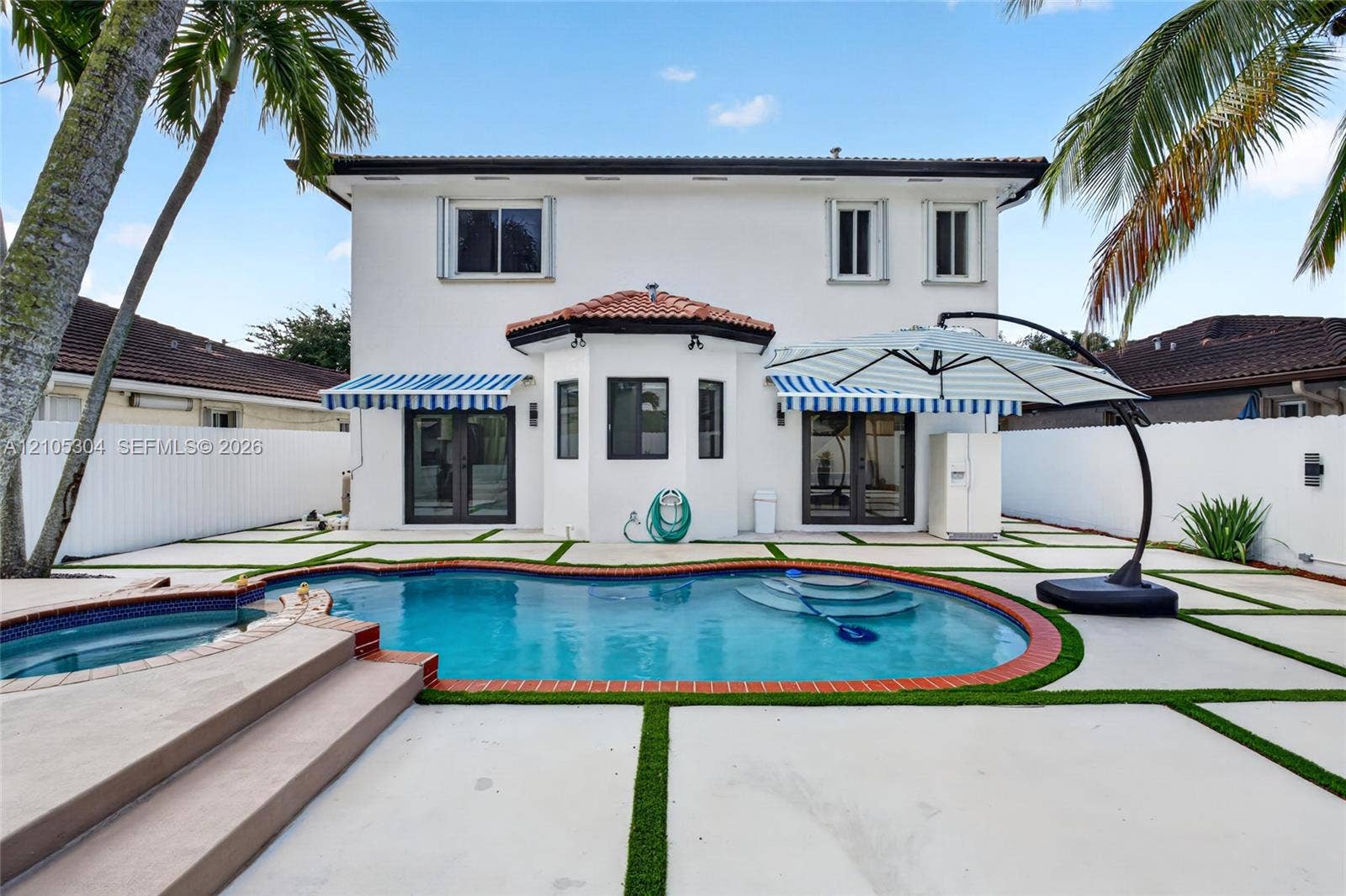 15217 SW 36th Terrace, Miami, FL 33185 Stucco exterior featuring a pool and elevated spa with brick coping, concrete paver patio with turf joints, and retractable fabric awnings
