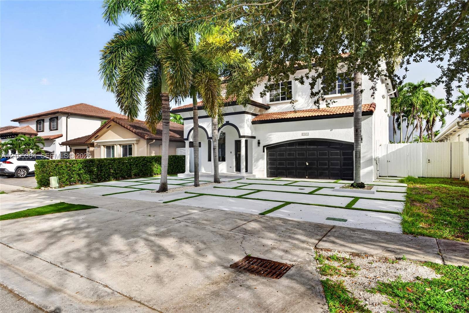 15217 SW 36th Terrace, Miami, FL 33185 Two-story exterior featuring white stucco finish, arched entryways, multi-car garage with dark metal doors, tile roof, and a paved driveway with integrated turf grid patterns