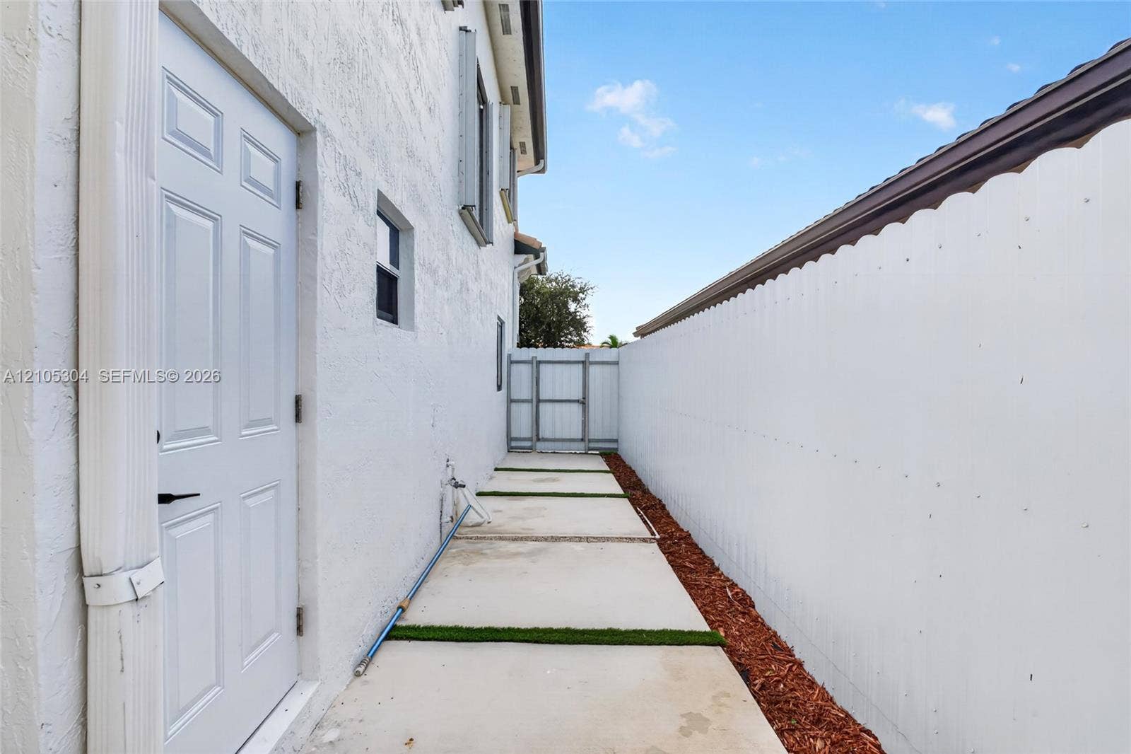 15217 SW 36th Terrace, Miami, FL 33185 Side exterior featuring a stucco facade, concrete paver path with grass inlay, mulched landscape border, solid perimeter wall, and gated entry