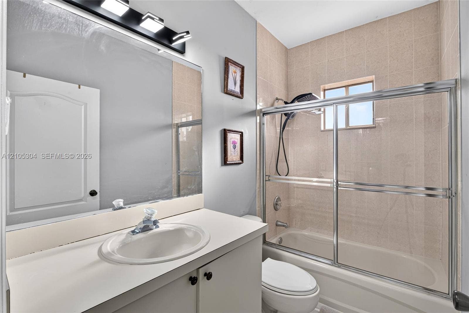 15217 SW 36th Terrace, Miami, FL 33185 Bathroom featuring a vanity with a white countertop and oval basin, wall-mounted vanity lighting, a full-width mirror, and a tub-shower combination with a sliding glass door and tiled surround